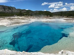 a pool of steaming blue water in the middle of rocky terrain
